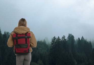 Image of Tourist with travel backpack enjoying foggy mountain forest during vacation trip