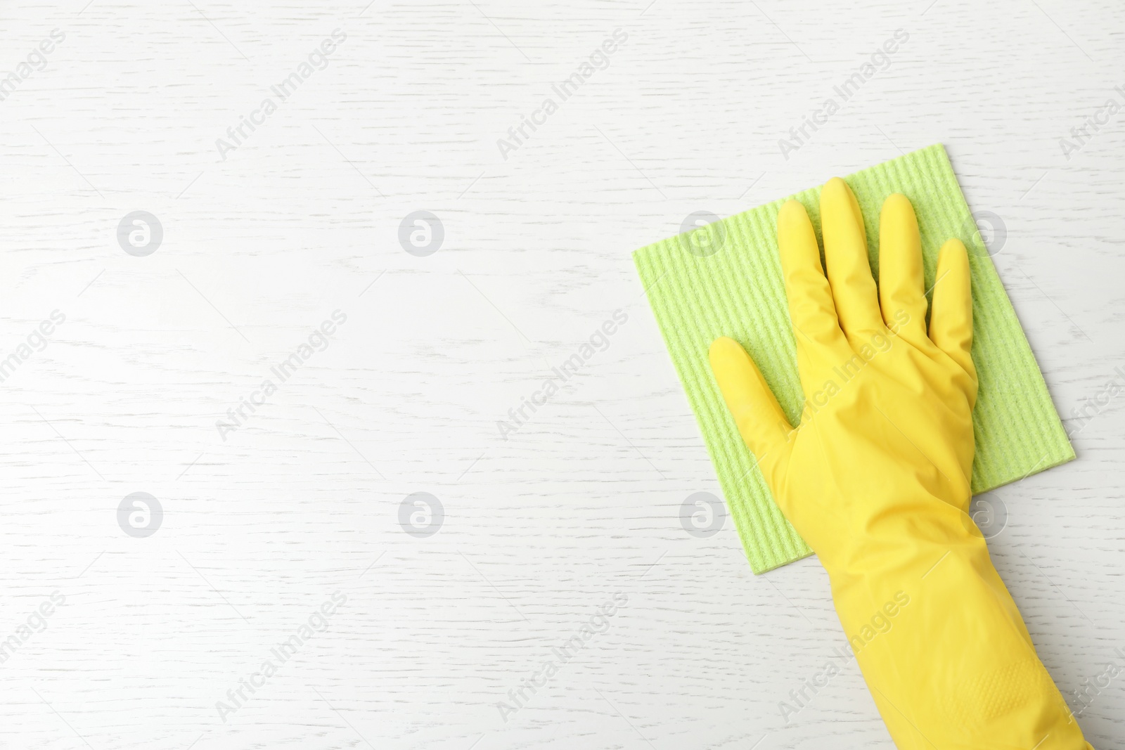 Photo of Person in gloves wiping white wooden table with rag, top view. Space for text