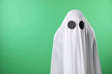 Photo of Creepy ghost. Person covered with white sheet on green background, space for text