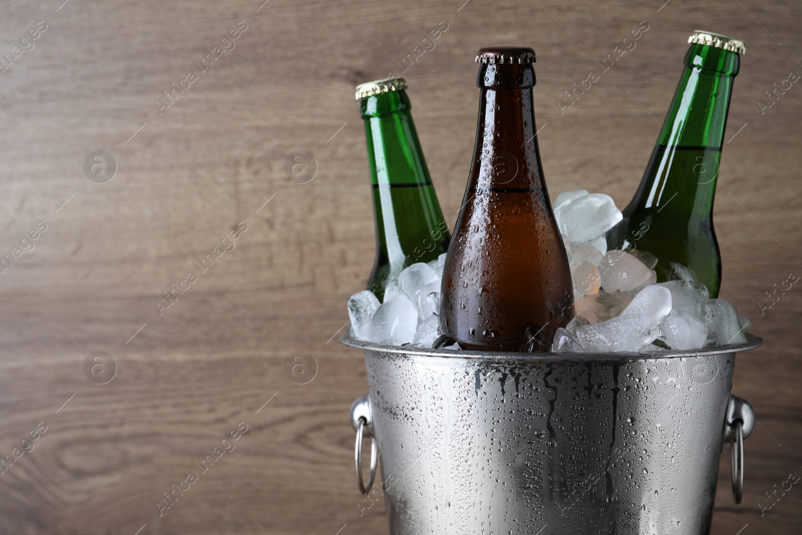 Photo of Metal bucket with bottles of beer and ice cubes on wooden background, closeup. Space for text