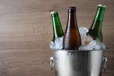 Metal bucket with bottles of beer and ice cubes on wooden background, closeup. Space for text