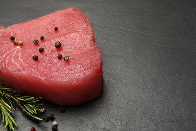 Photo of Raw tuna fillet with peppercorns and rosemary on black table. Space for text