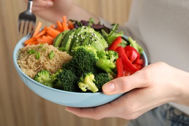 Woman holding vegan bowl with avocados, carrots and broccoli indoors, closeup