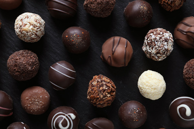 Photo of Different tasty chocolate candies on black table, flat lay