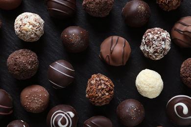 Different tasty chocolate candies on black table, flat lay