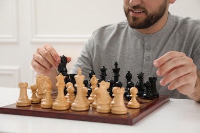Photo of Man playing chess at white table indoors, closeup