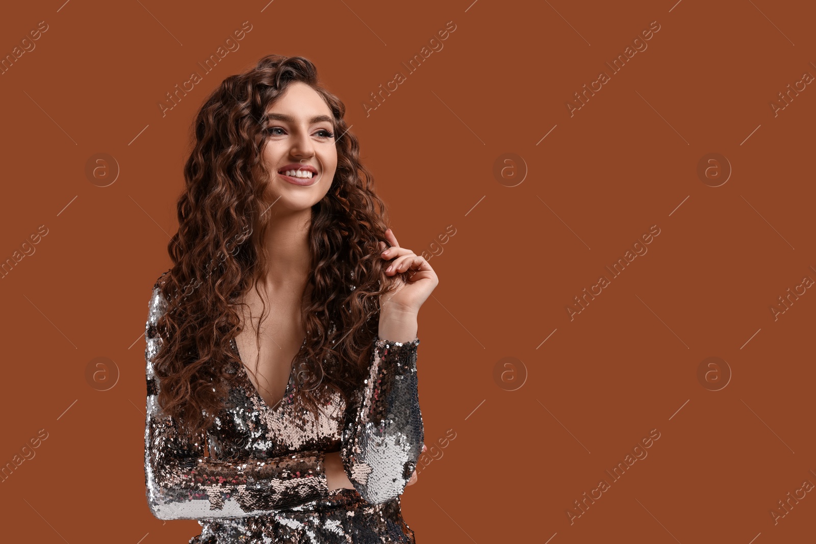 Photo of Beautiful young woman with long curly hair in sequin dress on brown background, space for text