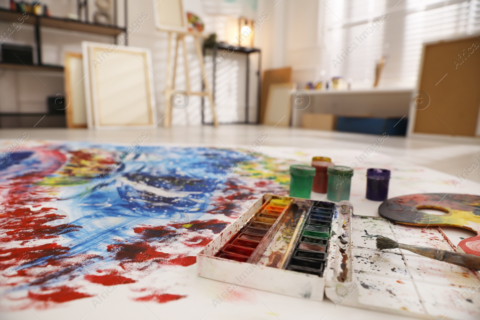 Photo of Paints and brush on abstract picture in art studio with easel