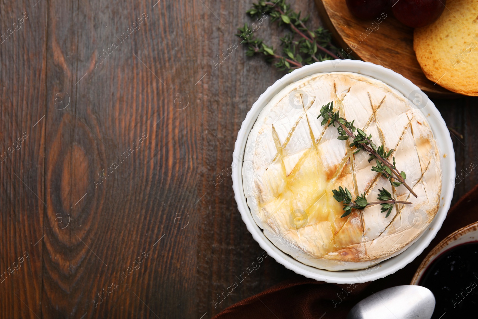 Photo of Tasty baked camembert and thyme in bowl on wooden table, flat lay. Space for text