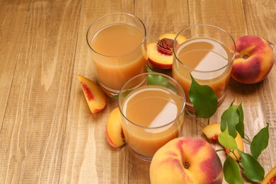 Photo of Glasses of peach juice, fresh fruits and leaves on wooden table. Space for text
