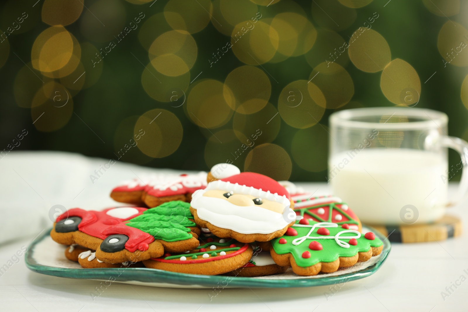 Photo of Decorated cookies and milk on white against blurred Christmas lights