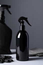 Photo of Spray bottles, black glove and rag on white table. Car products
