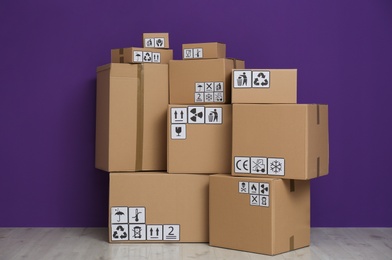 Cardboard boxes with different packaging symbols on floor near purple wall. Parcel delivery