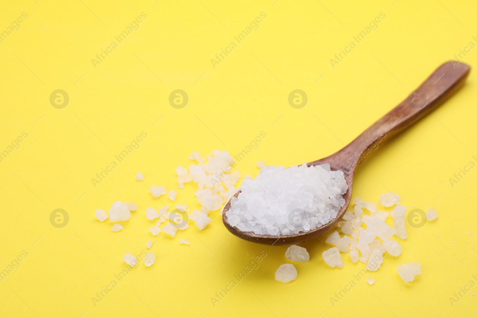 Photo of Spoon with sea salt on yellow background. Space for text