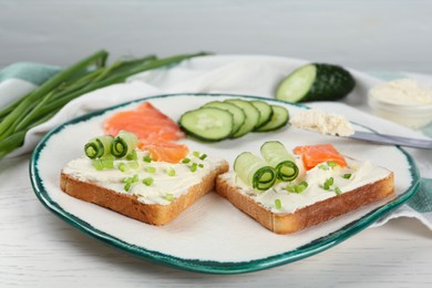 Photo of Toasted bread with cream cheese, salmon and cucumber on white wooden table