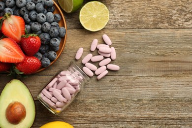 Vitamin pills in bottle and fresh fruits on wooden table, flat lay. Space for text