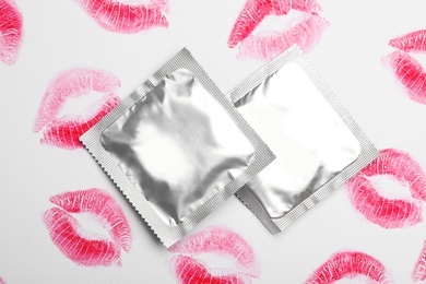 Photo of Condoms and lipstick kiss marks on white background, top view. Safe sex