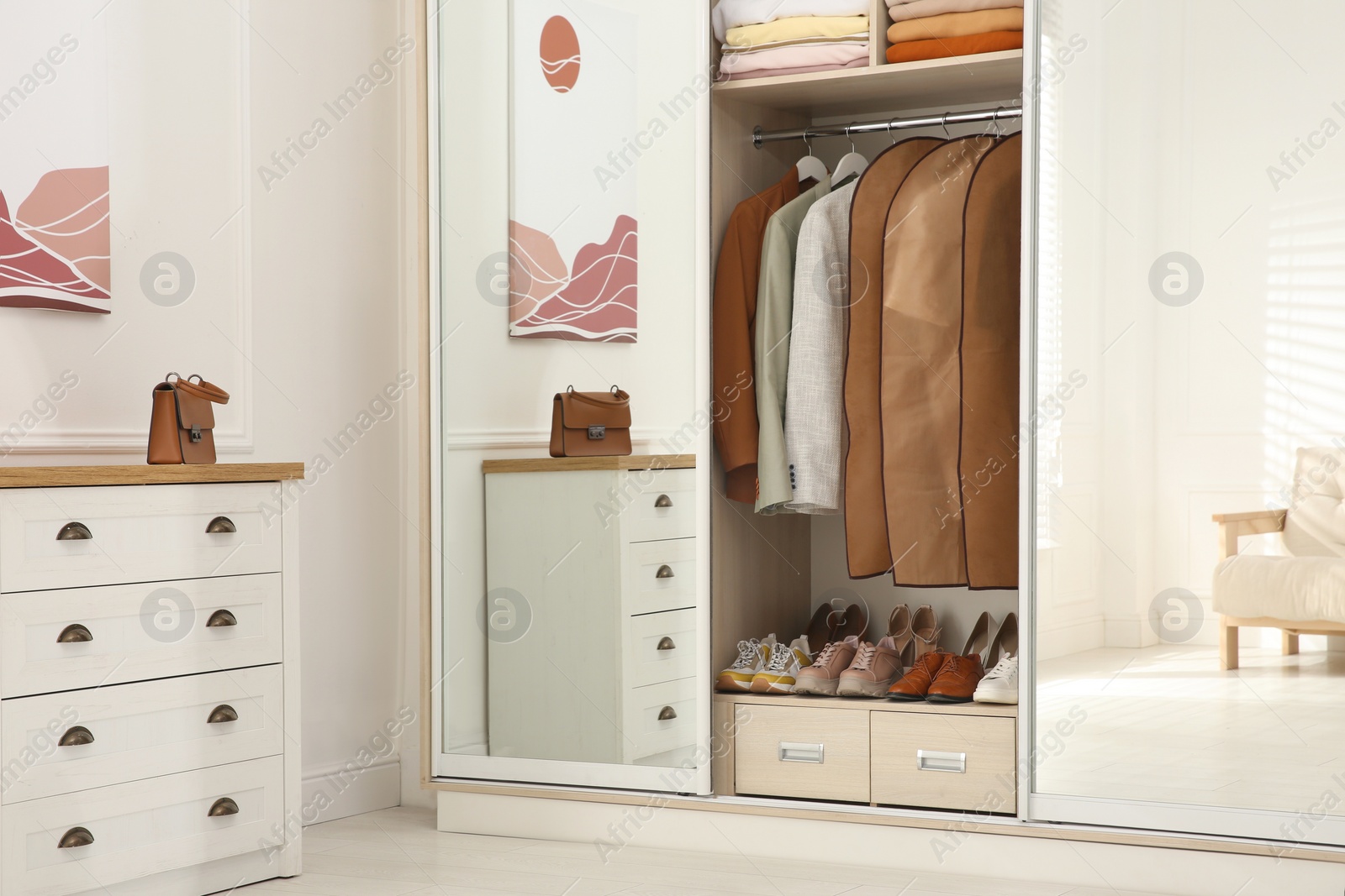 Photo of Garment bags with clothes on rack in wardrobe indoors