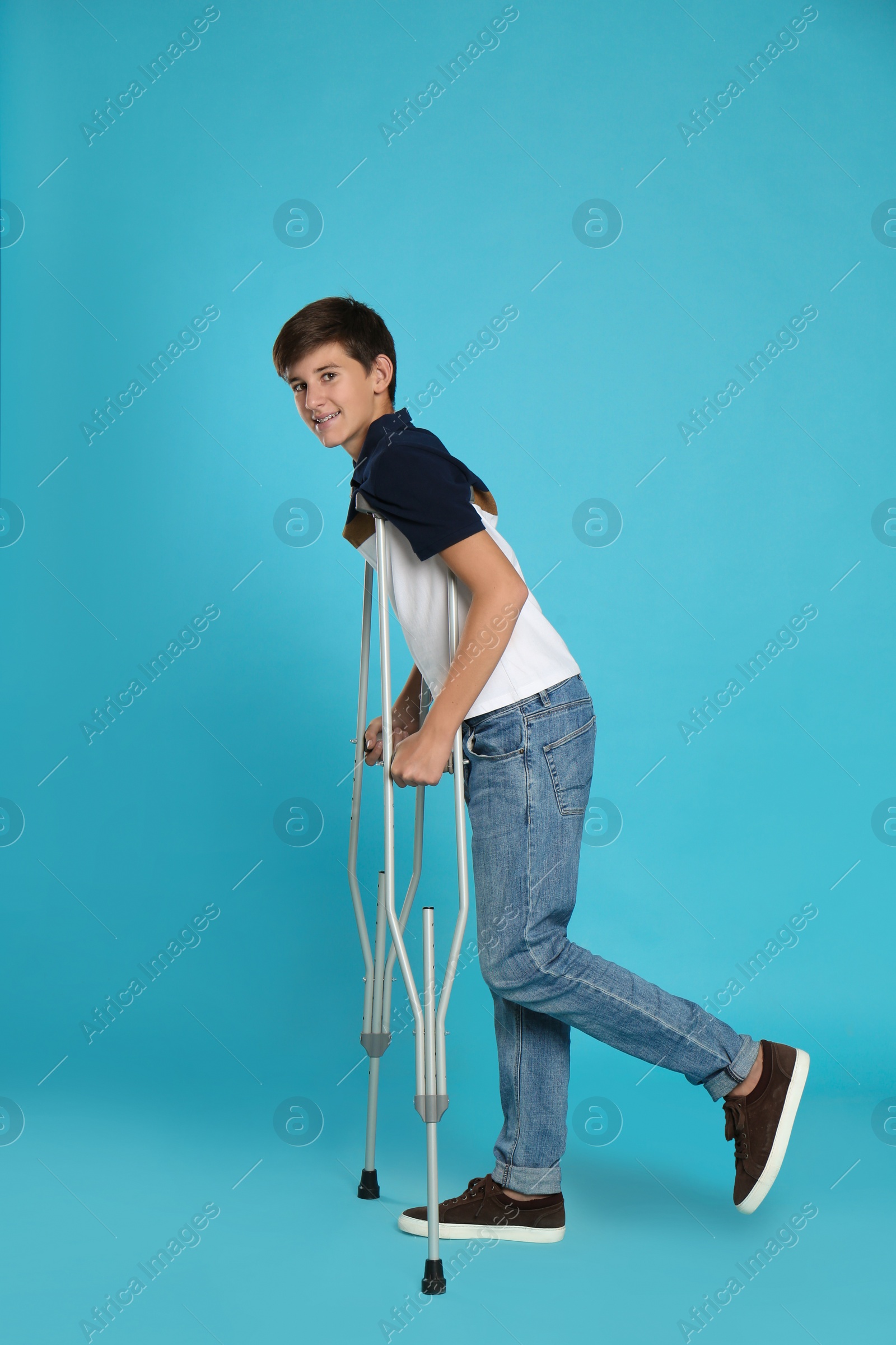 Photo of Teenage boy with injured leg using crutches on turquoise background