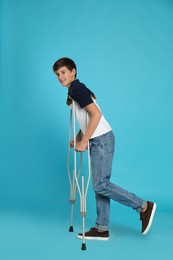 Photo of Teenage boy with injured leg using crutches on turquoise background