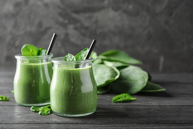 Jars of healthy green smoothie with fresh spinach on grey wooden table. Space for text