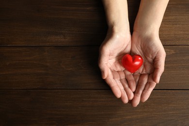 Photo of Elderly woman holding red heart in hands at wooden table, top view. Space for text