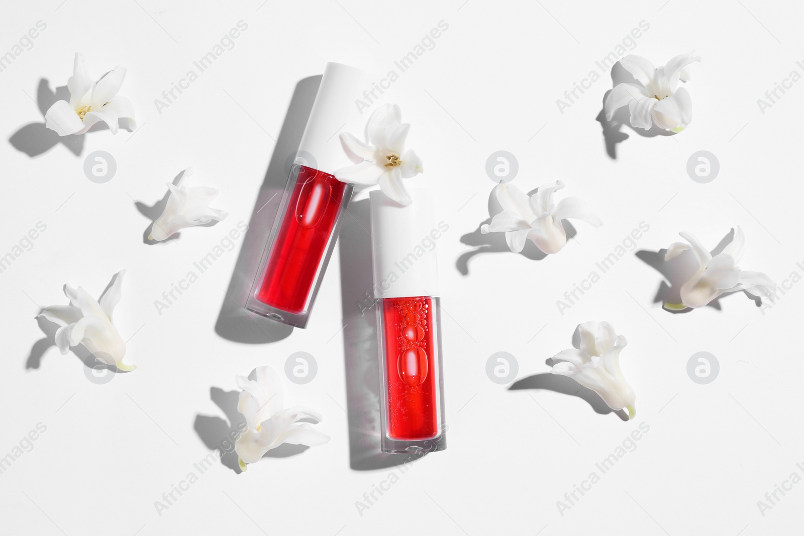 Photo of Bright lip glosses and flowers on white background, flat lay