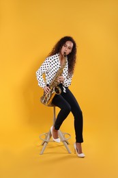 Beautiful African American woman playing saxophone on yellow background