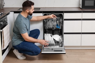 Photo of Man loading dishwasher with glasses in kitchen