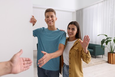 Photo of Happy couple welcoming their guest near white wall at home. Invitation to come in room