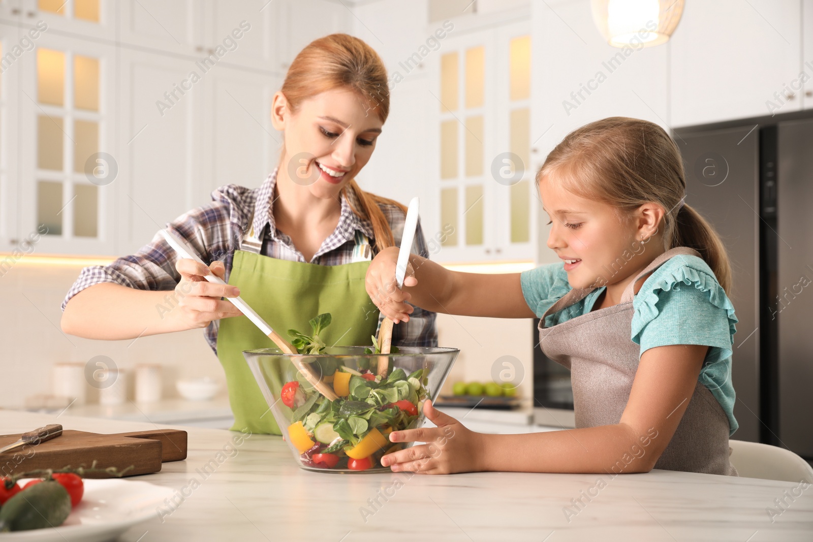 Photo of Mother and daughter cooking salad together in kitchen