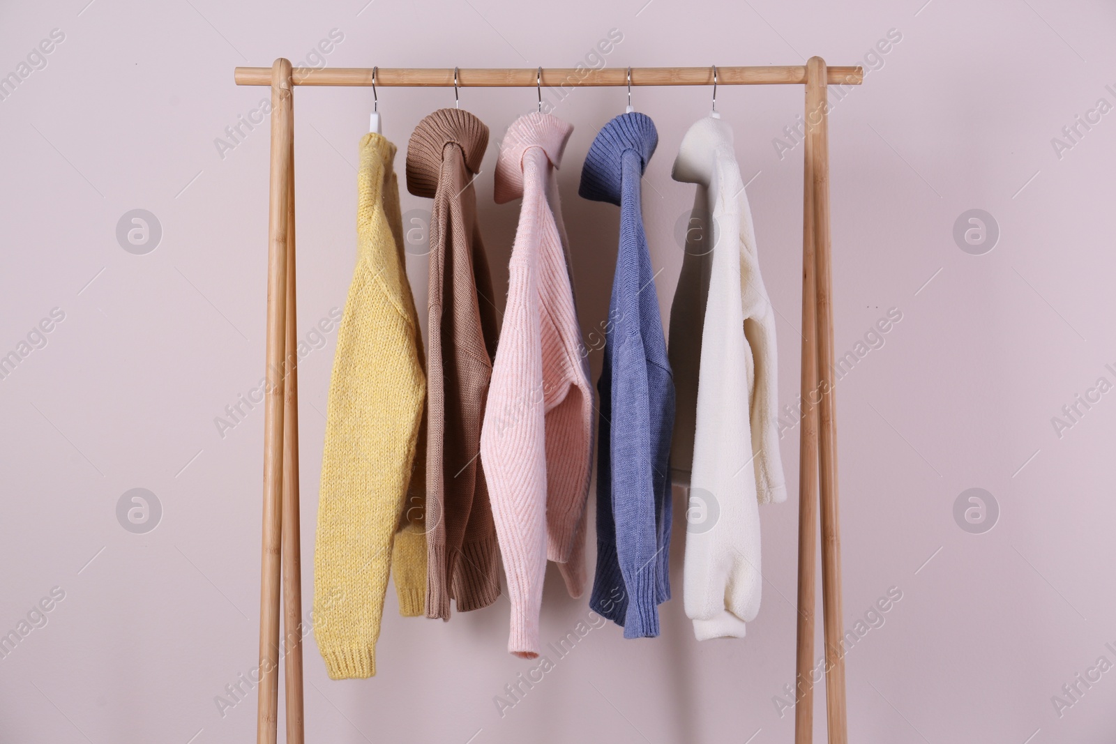 Photo of Warm sweaters hanging on wooden rack against pink background