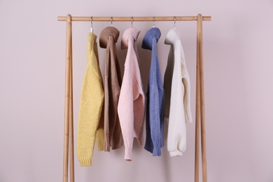 Photo of Warm sweaters hanging on wooden rack against pink background