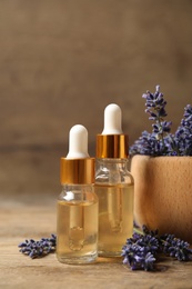 Beautiful lavender flowers and natural essential oil on wooden table, closeup