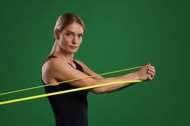 Athletic woman exercising with elastic resistance band on green background