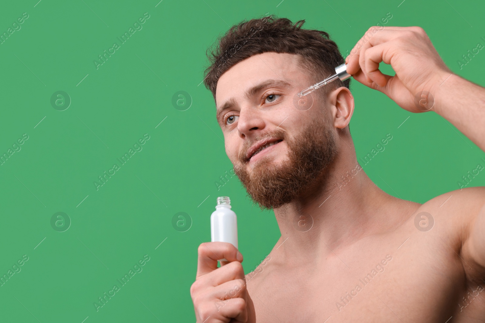 Photo of Handsome man applying serum onto his face on green background, space for text