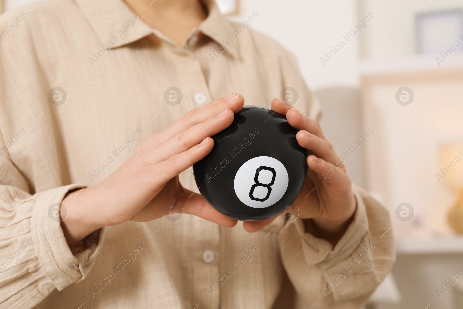 Photo of Woman holding magic eight ball indoors, closeup