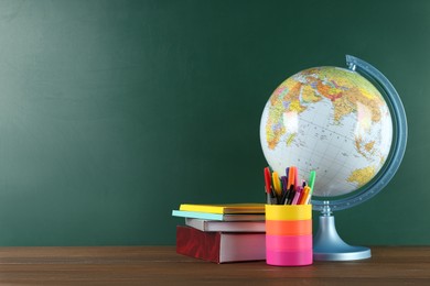 Globe, books and school supplies on wooden table near green chalkboard, space for text. Geography lesson