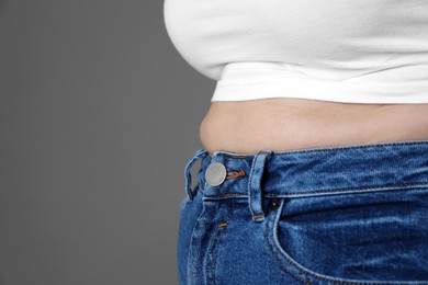 Overweight woman in tight shirt and jeans on grey background, closeup. Space for text