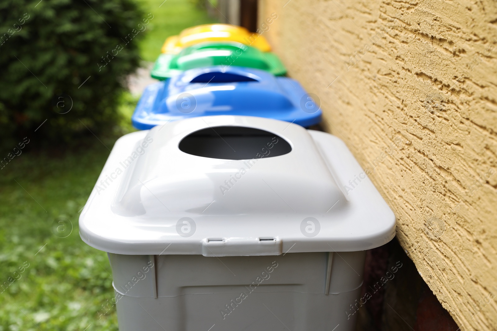 Photo of Many colorful recycling bins near yellow wall outdoors