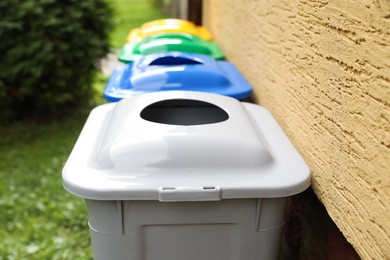 Many colorful recycling bins near yellow wall outdoors