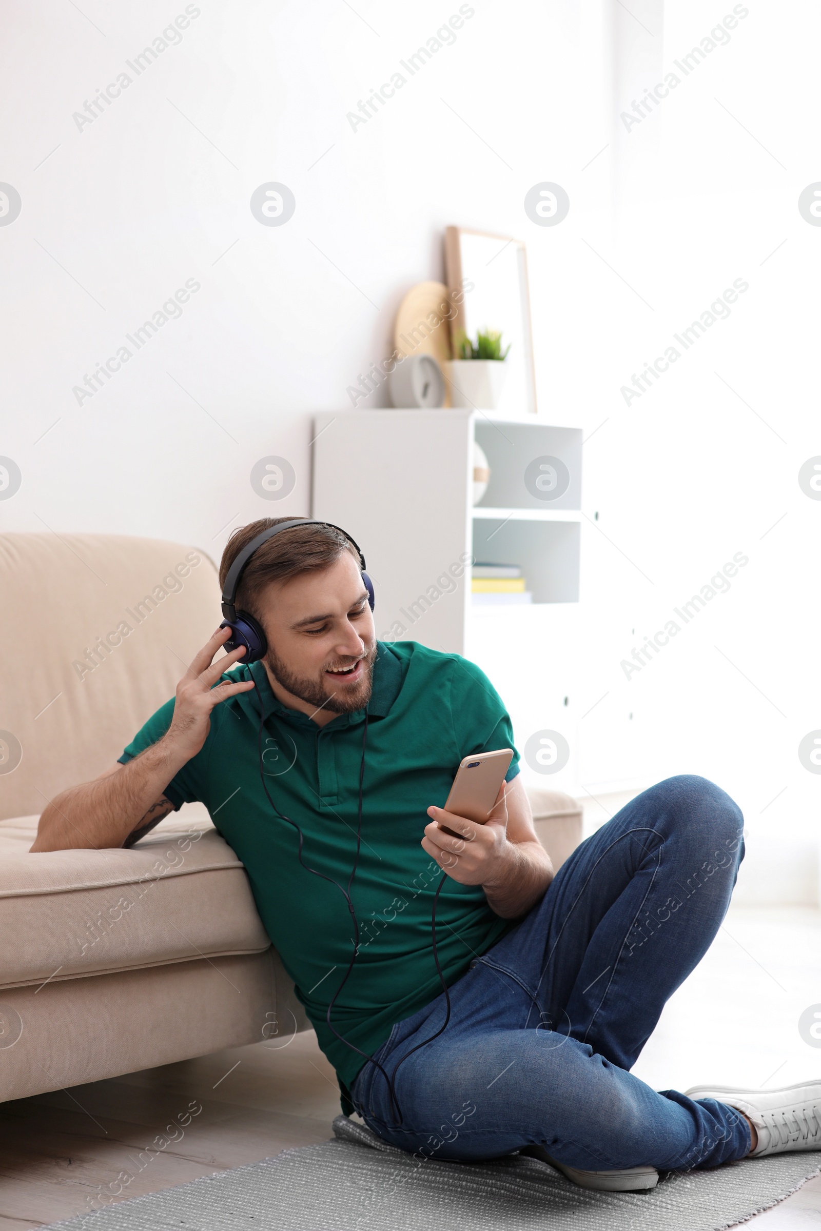 Photo of Young man in headphones with mobile device enjoying music at home