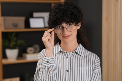 Photo of Portrait of beautiful woman in glasses indoors. Attractive lady with curly hair looking into camera