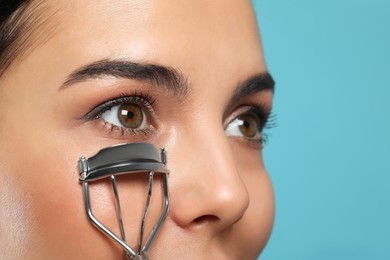 Young woman using eyelash curler on light blue background, closeup