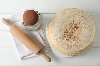 Photo of Tasty homemade tortillas, flour and rolling pin on white wooden table, top view