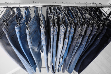 Photo of Rack with different jeans near light background, closeup