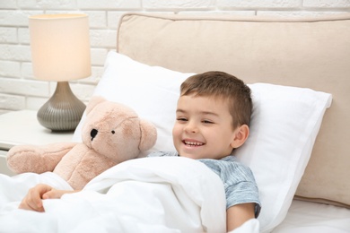Cute child with teddy bear resting in bed at hospital