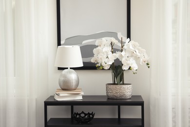 Photo of Blooming orchid and lamp on console table indoors. Interior design
