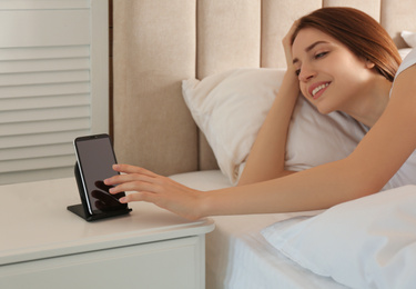 Woman taking smartphone from wireless charger in bedroom