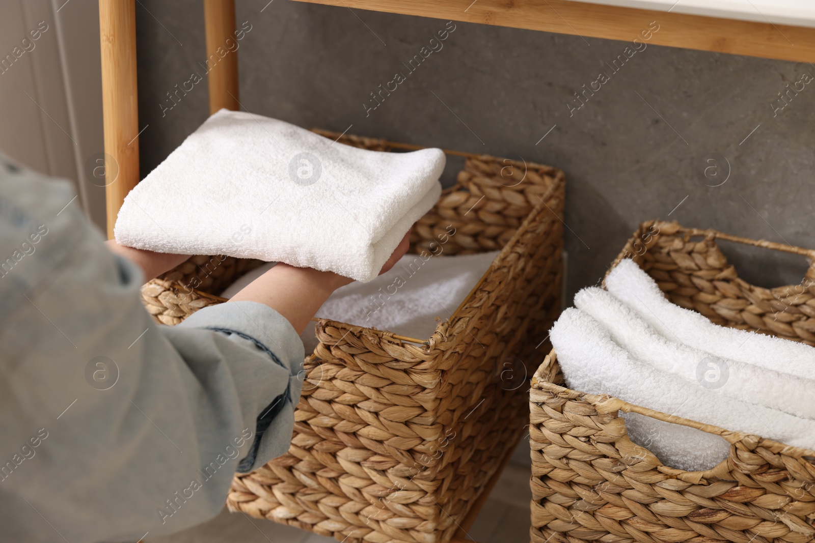 Photo of Woman putting towel into storage basket indoors, closeup